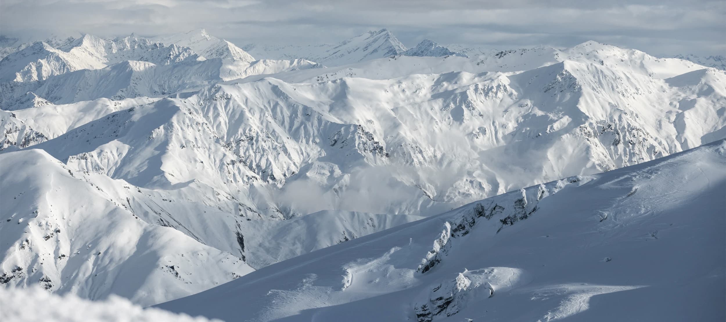 A breathtaking view of the snow-covered mountain ranges of Treble Cone, showcasing the expansive terrain and steep alpine features, perfect for skiing and snowboarding enthusiasts.