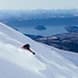 A person sends a plume of fresh powder downhill as they make fresh tracks through the snow.