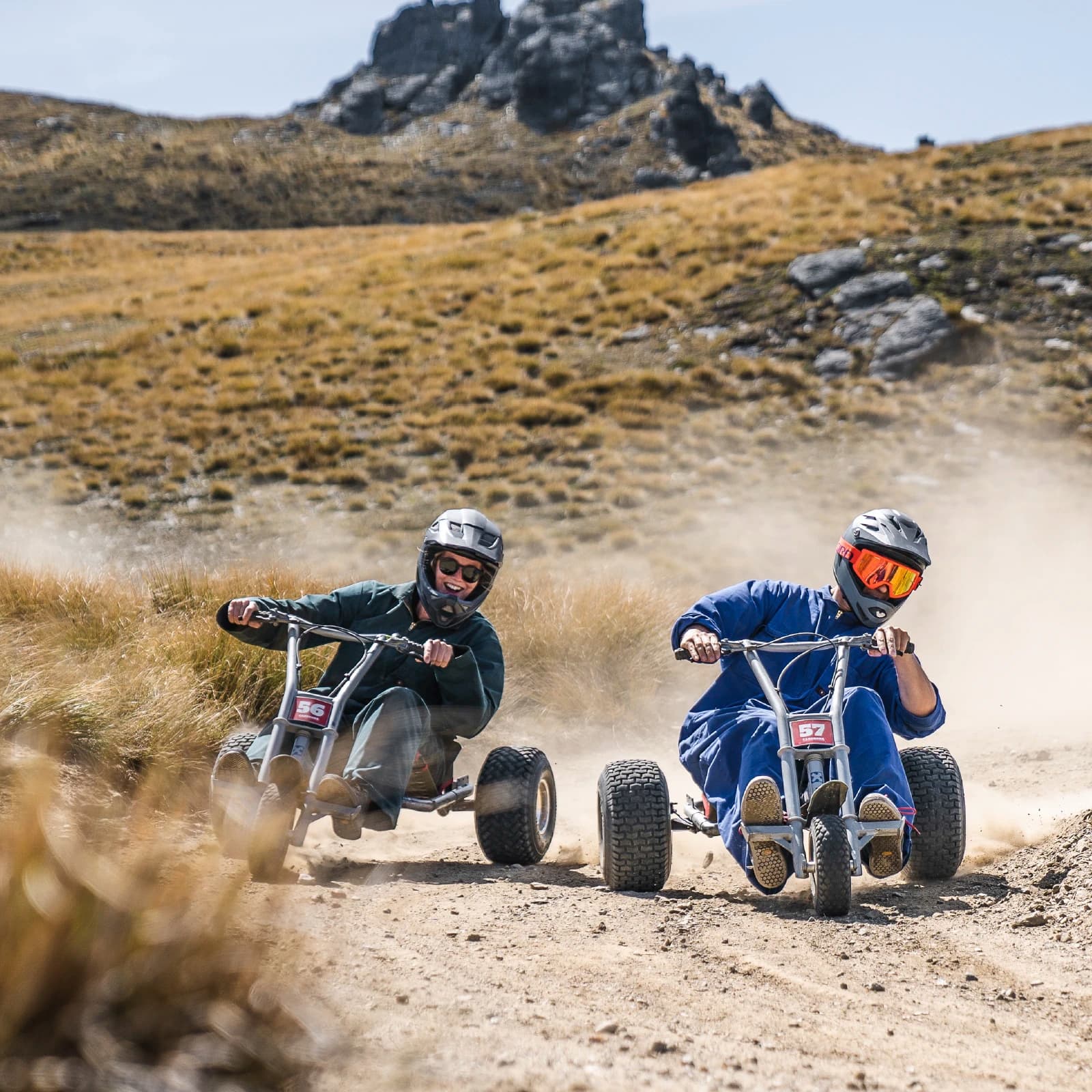 Two friends race around a corner on a mountain cart at Cardrona.