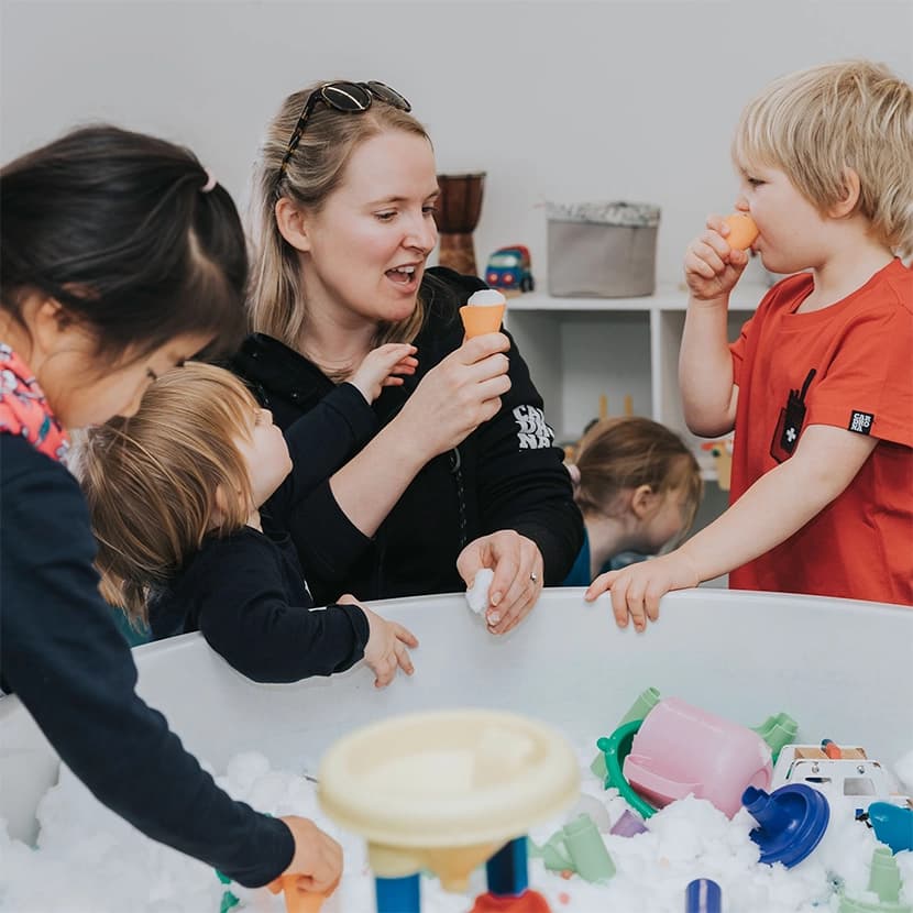 A childcare worker at Cardrona Ski Kindy engages with young children in a playful activity, using toy cones and snow, creating a fun and interactive environment for the kids.