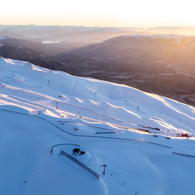 An expansive view of a snow-covered ski resort at sunrise, with soft light illuminating the slopes and surrounding mountain landscape.