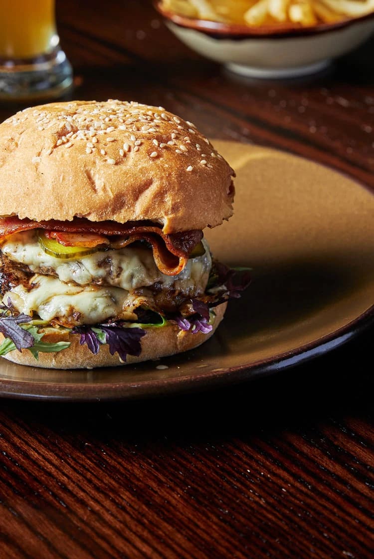 A delicious double beef burger with fries and a drink on the side.