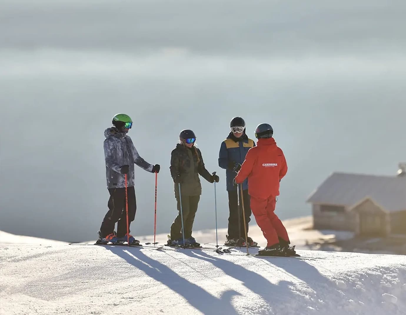 A group of skiers listening to an instructor in red on a mountain.