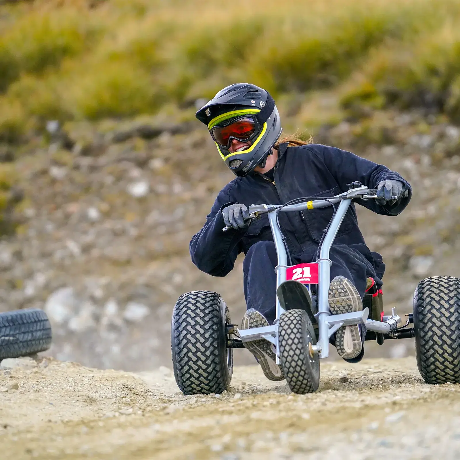 Person riding a mountain cart on a gravel track at Cardrona, wearing a helmet and goggles.
