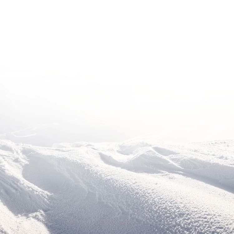 A serene, snow-covered mountain landscape, with soft, undulating slopes bathed in a misty haze.
