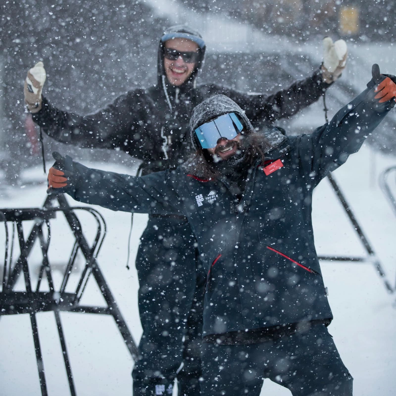 Two staff members raise their hands as fresh snow lands around them.