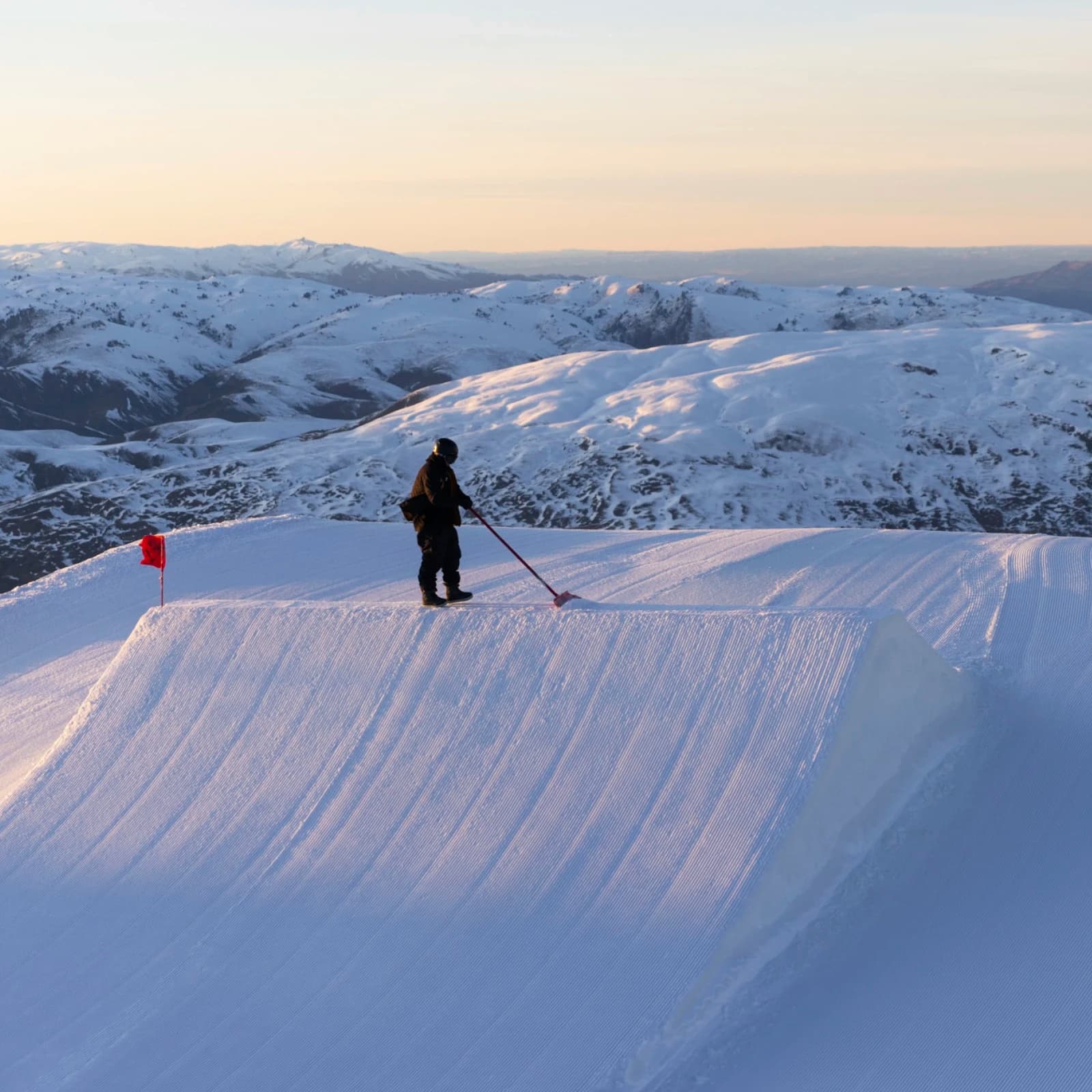 A serene early morning scene at a ski resort with a park crew member grooming a perfectly shaped jump.