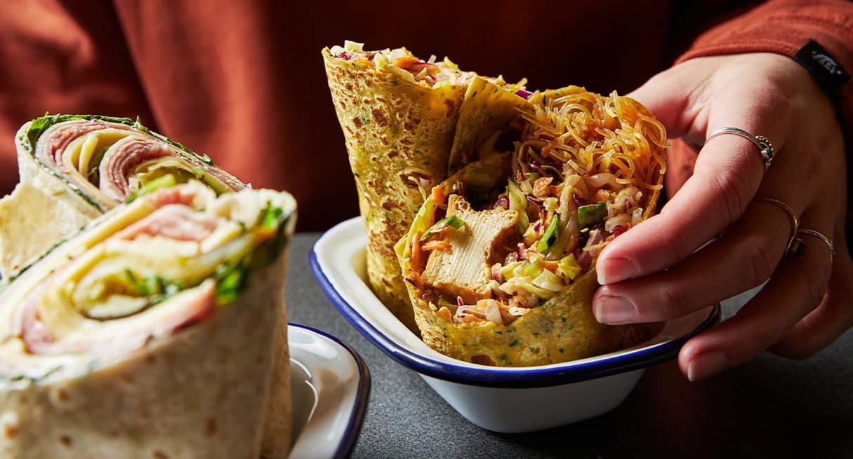 A person picks up a chicken wrap cut in half from a metal plate.