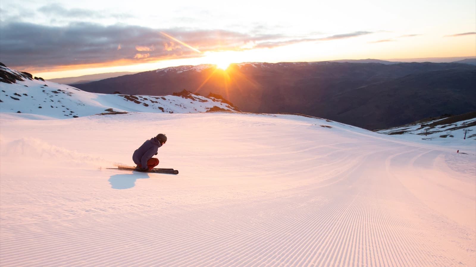 Skier cruising freshly groomed corduroy at sunrise, soaking up golden spring light in the Southern Alps.