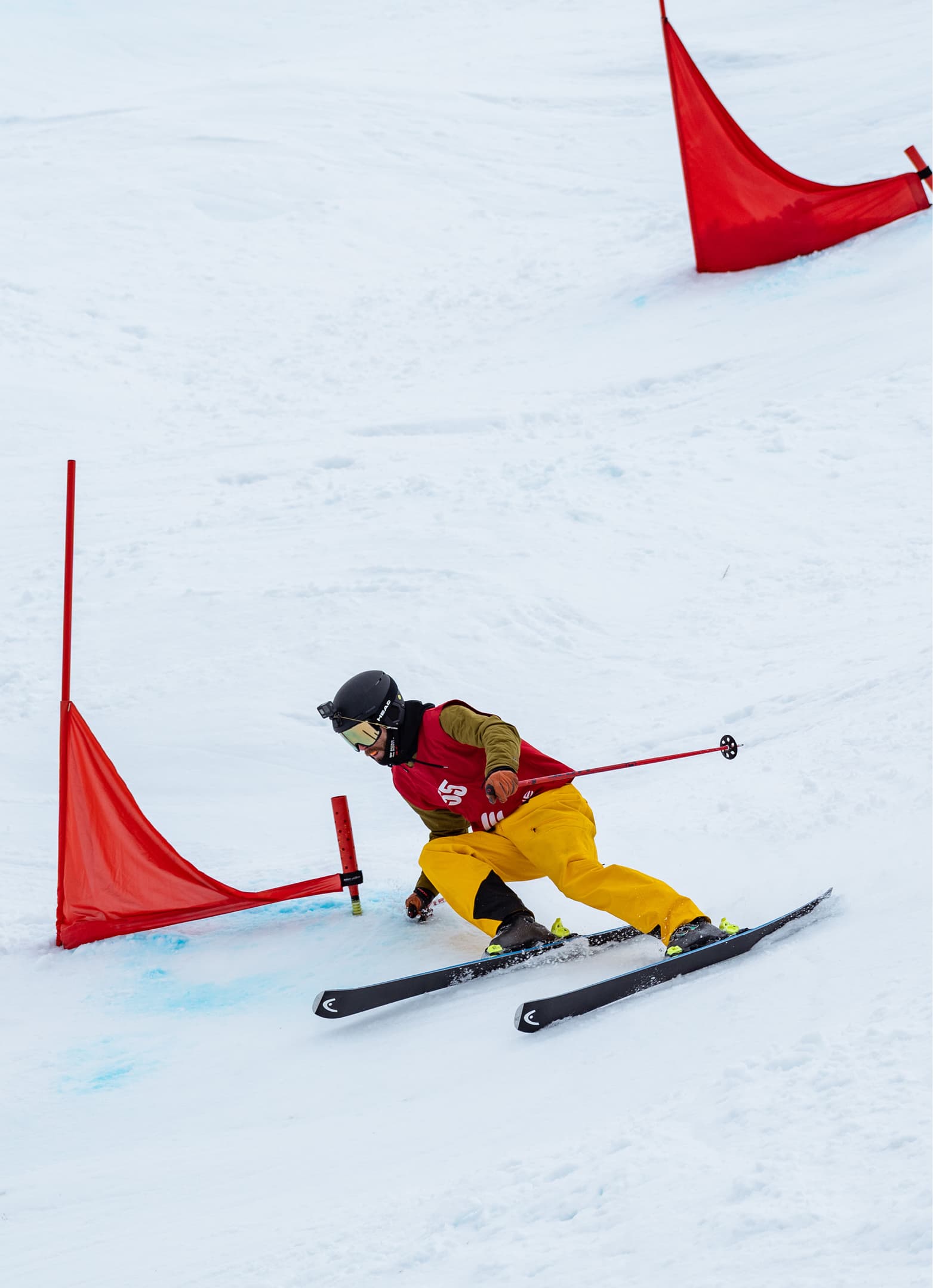 Skier in yellow pants navigating through a slalom course with red gates on a groomed slope, leaning into the turn.