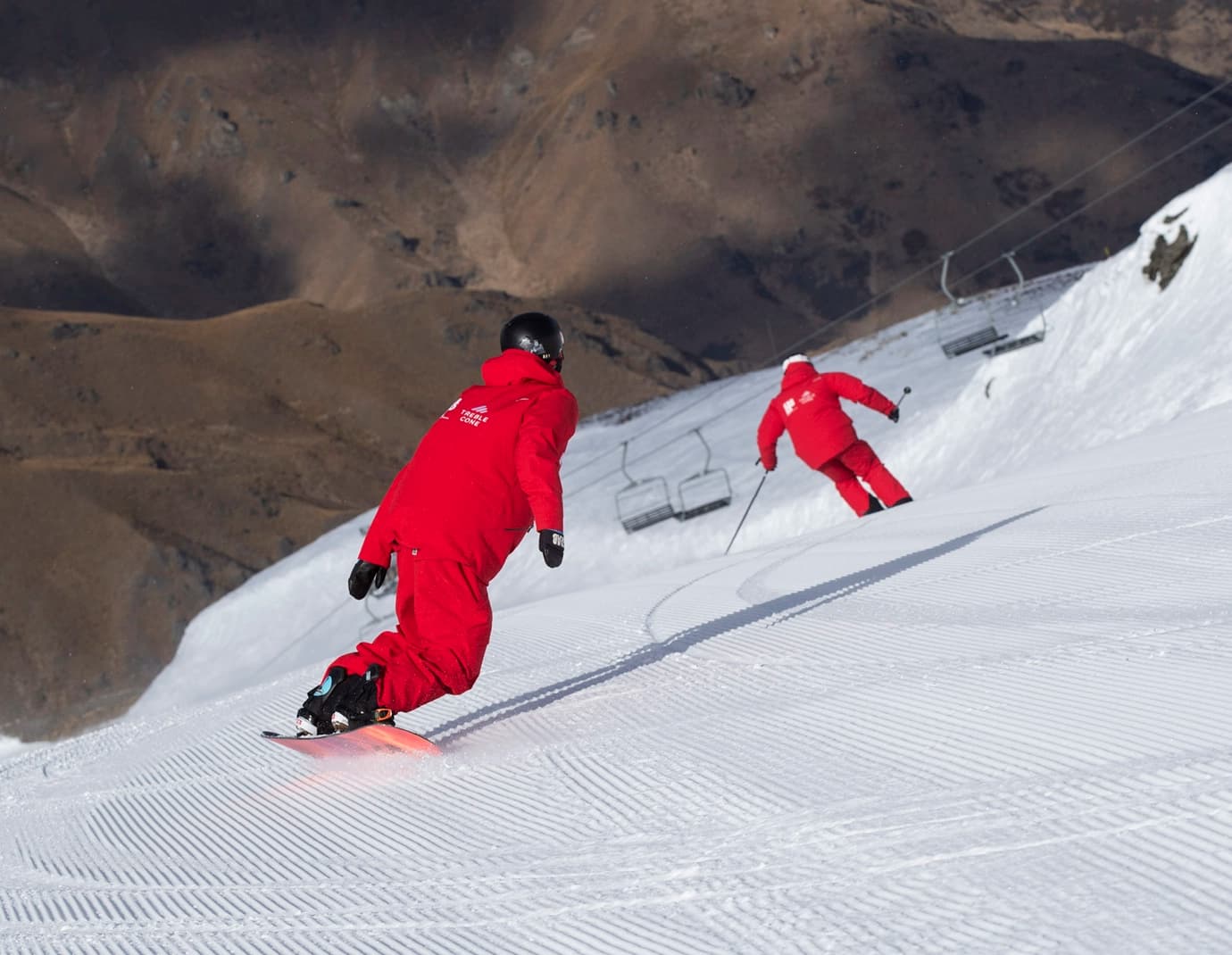 Two ski instructors ride down a run together in full red uniform.
