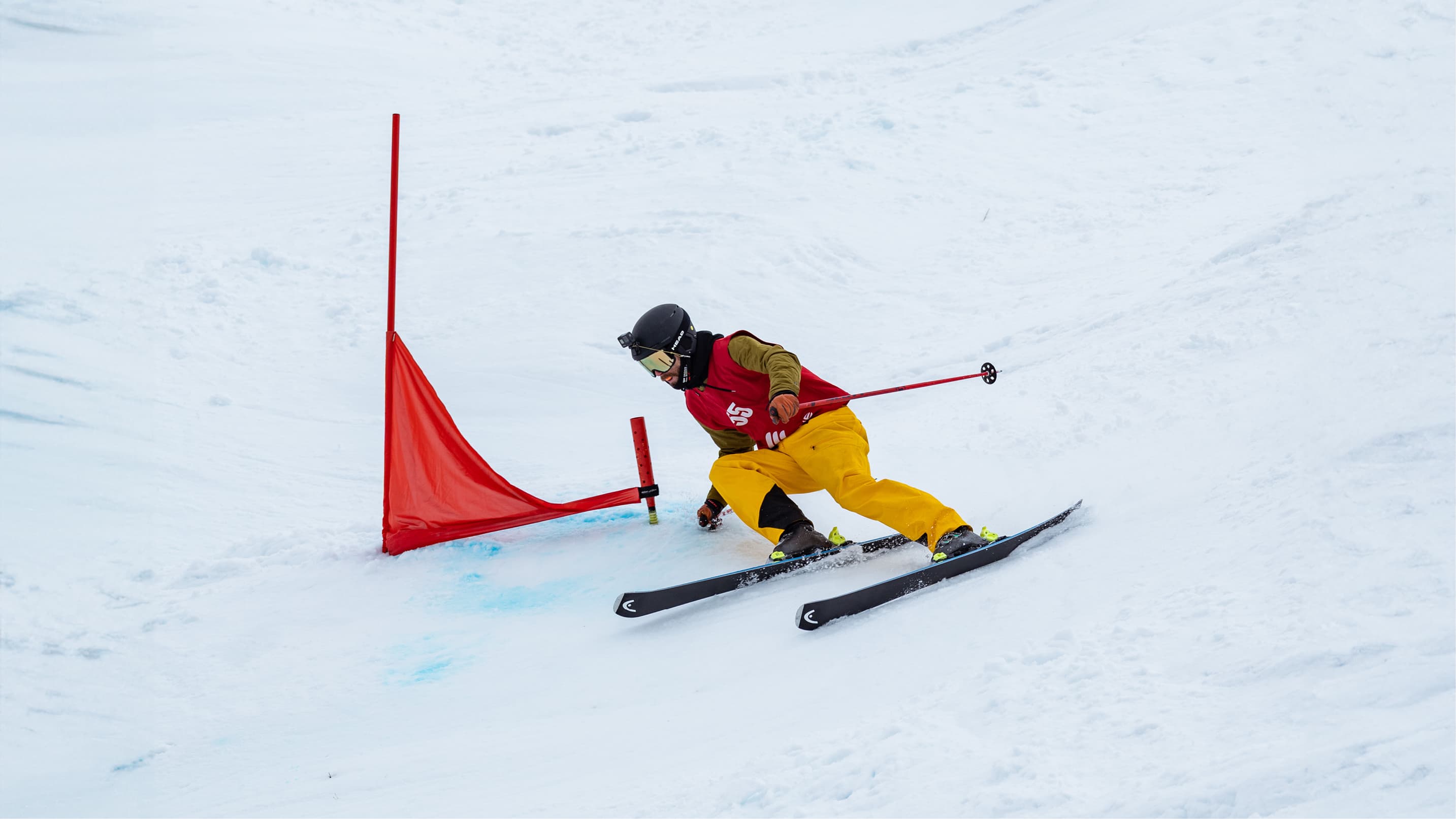 Skier in yellow pants navigating through a slalom course with red gates on a groomed slope, leaning into the turn.