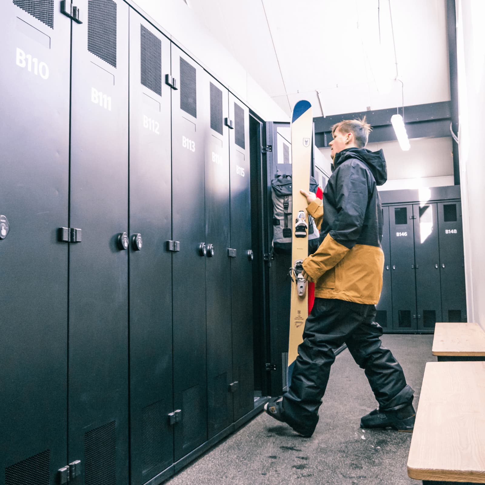 A man in full snow gear puts his skis into a full length locker.